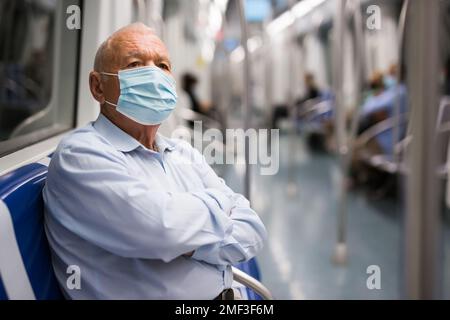 Old man in face mask sitting inside subway train Stock Photo