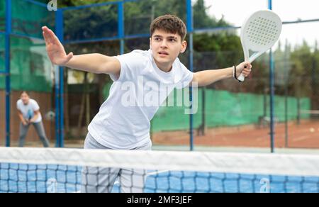 Sportive young man holding padel racquet in hand and ready to return ball while playing in court Stock Photo