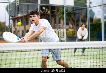 Guy hitting two handed backhand during paddle tennis match Stock Photo