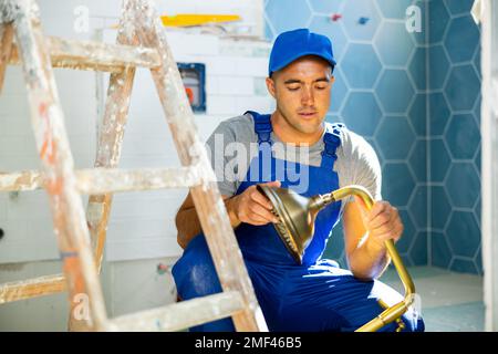 Experienced repairman in work clothes replacing plumbing in bathroom mounting shower shower holder with height adjustable shower head Stock Photo