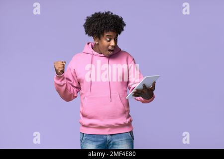 Surprised excited African teen guy winner student boy looking at digital tablet. Stock Photo