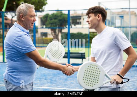 Two men shake hands after playing padel on tennis court Stock Photo
