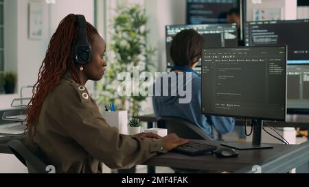 African american software engineer working focused on programming it language at computer, typing html script. Database programer writing code with algorithms on terminal window. Stock Photo
