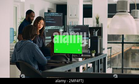 Team of programmers working on source code with greenscreen monitor in cloud computing office. App developers checking isolated chromakey display with copyspace and html script. Tripod shot. Stock Photo