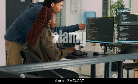 Two software coders analyzing source code on computer and laptop screen, using html script on terminal window. Team of system engineers working on cyber security innovation in it agency. Stock Photo