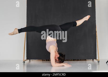 Young professional gymnast woman standing on splits. Pretty brunette girl doing an elbow stand. Female athlete doing warm-up before training. Copy spa Stock Photo