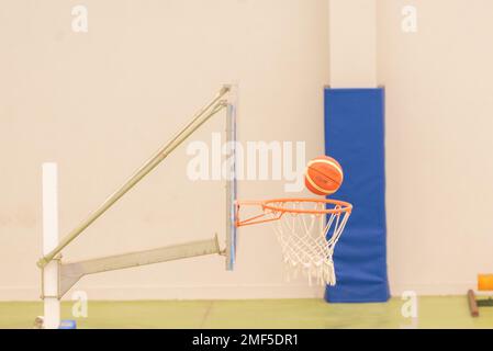 side view of a basketball entering a mini-basketball basket on a court without parquet, green colour Stock Photo