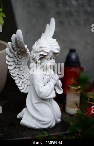 small white praying angel figure on a grave with grave candles in blurred background Stock Photo