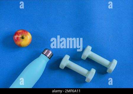 Top view of dumbbells, bottle with water and apple on blue sports mat. Flat lay, copy space. Healthy lifestyle, dieting, home training concept. Stock Photo