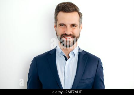 Close-up photo of a confident handsome bearded caucasian businessman, corporate executive, ceo, in formal elegant suit, stand on isolated white background, looks at camera, smiling friendly Stock Photo