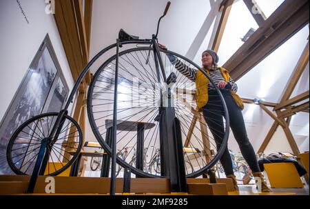 Wismar, Germany. 24th Jan, 2023. A woman stands in front of a penny-farthing bicycle from around 1890 in the new permanent exhibition of more than 50 historic two-wheelers at the Phantechnikum. As an extension of its permanent exhibition, the Museum of Technology will open a focus on the technical and cultural history of the bicycle on Jan. 25, 2023. The bicycles from the holdings of a collector from Wismar illustrate milestones in the genesis of the bicycle and link these with regional historical stories about cycling. Credit: Jens Büttner/dpa/Alamy Live News Stock Photo