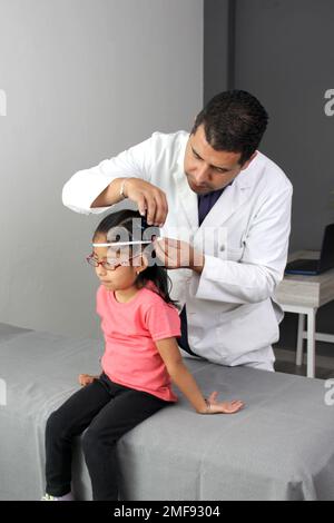 Latino pediatrician specialist doctor measures the head of his patient, a small 4-year-old brunette girl checks her measurements during medical check Stock Photo