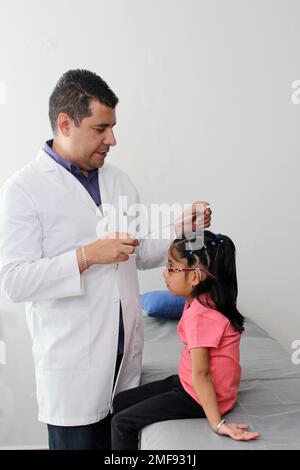 Latino pediatrician specialist doctor measures the head of his patient, a small 4-year-old brunette girl checks her measurements during medical check Stock Photo