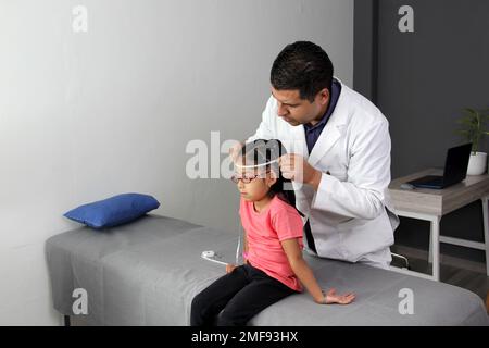 Latino pediatrician specialist doctor measures the head of his patient, a small 4-year-old brunette girl checks her measurements during medical check Stock Photo