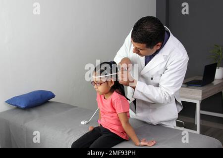 Latino pediatrician specialist doctor measures the head of his patient, a small 4-year-old brunette girl checks her measurements during medical check Stock Photo