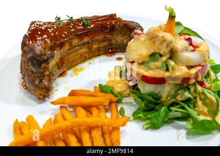 Die cut of grilled smoked ribs with barbeque sauce, potato and vegetable salad on white isolated. Stock Photo