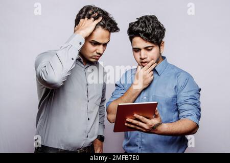 Sad despaired young Indian male managers looking at tablet screen, find mistake in office accounts. Problems in business, work planning, finance, data Stock Photo