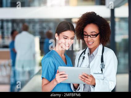 I am happy the results turned out the way they have. two cheerful young doctors working on a digital tablet together while standing in the hospital Stock Photo