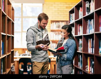 Doing as much research as they can together. two university students working together in the library at campus. Stock Photo
