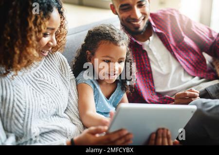Shes already a pro in handling technology. an adorable little girl using a digital tablet with her parents in their living room at home. Stock Photo