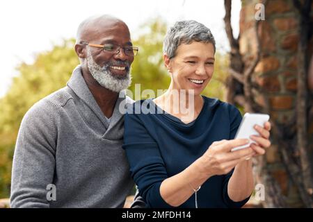 Getting to grips with modern technology. an affectionate senior couple using a cellphone while sitting in the park. Stock Photo