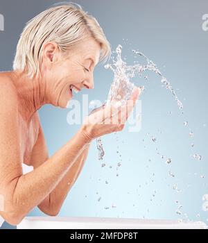 Senior woman, cleaning face and water splash on studio background for beauty, wellness and shower. Happy model, facial skincare drops and washing in Stock Photo