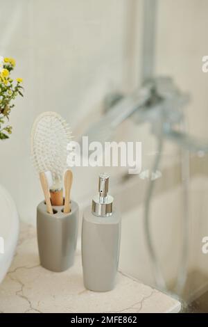 Liquid soap dispenser and cup with toothbrushes next to sink in bathroom Stock Photo