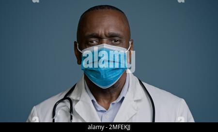 Serious african american mature man doctor surgeon therapist in medical gown and protective mask looking at camera posing in studio gray background Stock Photo