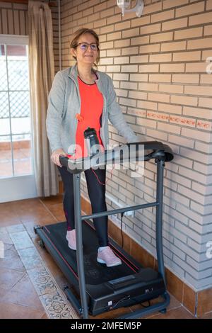 Mature white woman walking on a gymnastics machine to stay in shape and play sports. Stock Photo