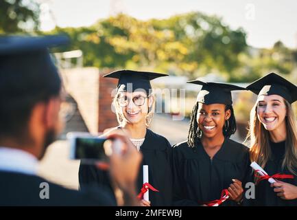 On three, everybody say, graduation. a group of students taking pictures with a mobile phone on graduation day. Stock Photo