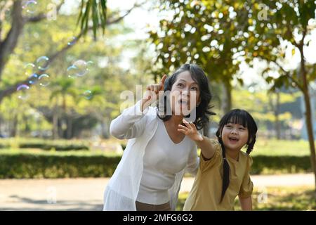 Grandmother and granddaughter having fun blowing soap bubbles into the air. Family, generation and people concept Stock Photo