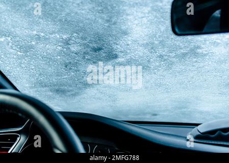 Frozen car windshield covered with ice and snow on a winter day. Selective focus. Stock Photo