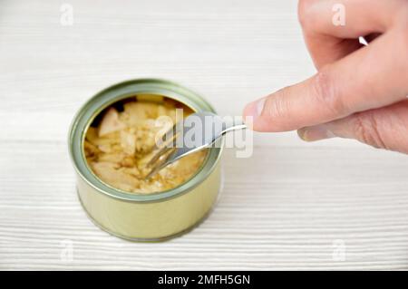Cropped shot of a man eating a canned of tuna on rustic wooden table Stock Photo