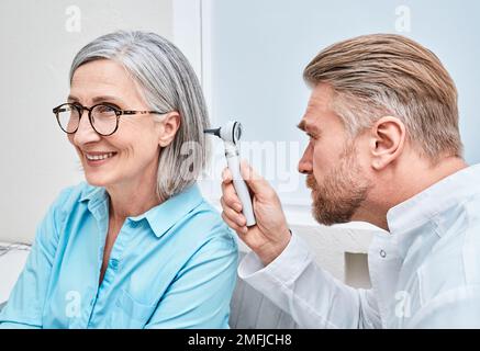 Otolaryngologist doctor checking mature woman's ear using otoscope or auriscope at ENT clinic. Hearing exam Stock Photo