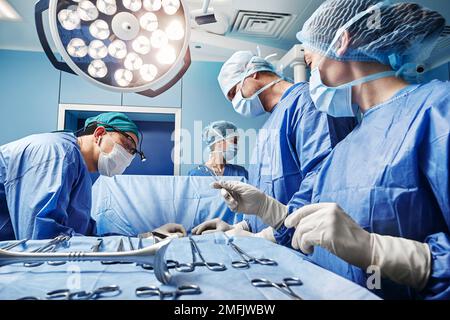 Surgical nurse giving surgical scissors to male surgeon during operation in operating theatre. Surgical Team Stock Photo