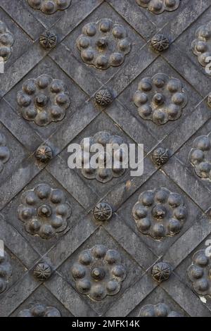An old metal door, forged gates, rivets on the facade of a cast-iron door, a round handle to open the door, the texture of old iron. High quality phot Stock Photo