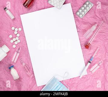 On a pink background, various medical items - pills, ampoules.  In the center is a blank white sheet for notes. Stock Photo