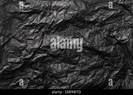 Flat lay view of black color crumpled package filling silk paper, products advertising background, studio light and shot. Lot of copy space. Stock Photo