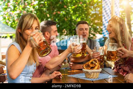 Friends, three men, two women, sitting in beer garden with beer glasses toasting to each other in Bavaria, Germany Stock Photo
