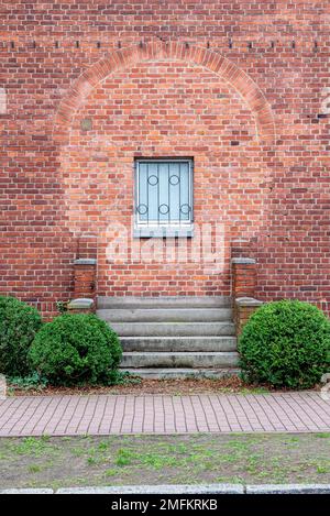 A red brick wall with a window, where before a door was bricked up. The stairs and the brick railing are still present Stock Photo