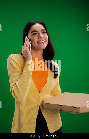 happy young woman calling on smartphone while standing with pizza box isolated on green,stock image Stock Photo