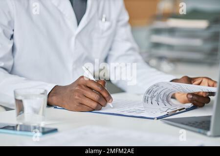 Close up of black doctor filling papers at desk in office while working in clinic, copy space Stock Photo