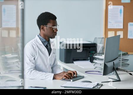 Side view portrait of young black doctor using computer at desk in office while working in private clinic Stock Photo