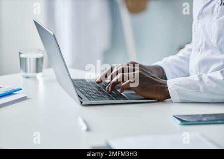 Minimal closeup of black doctor using laptop in office, focus on male hands typing at keyboard, copy space Stock Photo