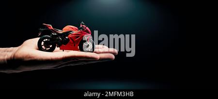 red sportbike model in hand on dark background. buy or rent a motorcycle. banner with copy space Stock Photo