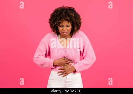 Sad pretty young black curly woman in casual suffering from stomach hurt, menstrual pain Stock Photo