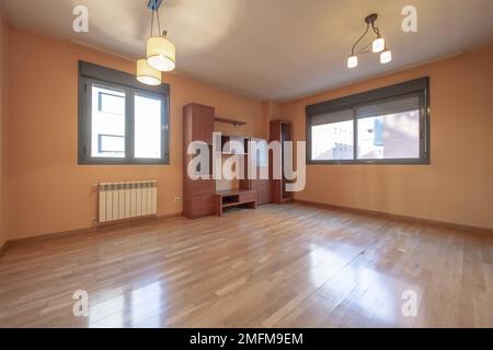 Empty living room with a small bookcase in the corner above shiny hardwood floors and anodized aluminum windows on several walls Stock Photo