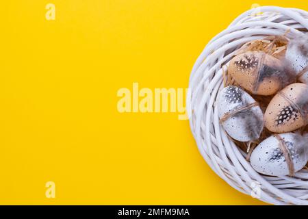 Easter composition with a decorative white wreath, quail eggs in the form of a nest on a yellow Stock Photo