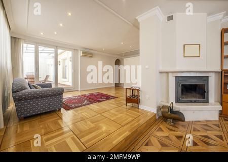 Long living room with two heights, wonderful wooden floors with inlaid wood, several upholstered sofas and a fireplace with a glass door Stock Photo