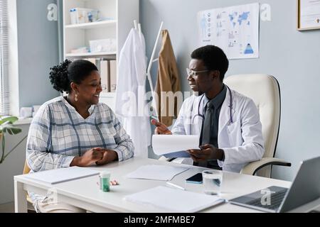 Portrait of young black doctor talking to young woman during consultation in clinic and smiling Stock Photo